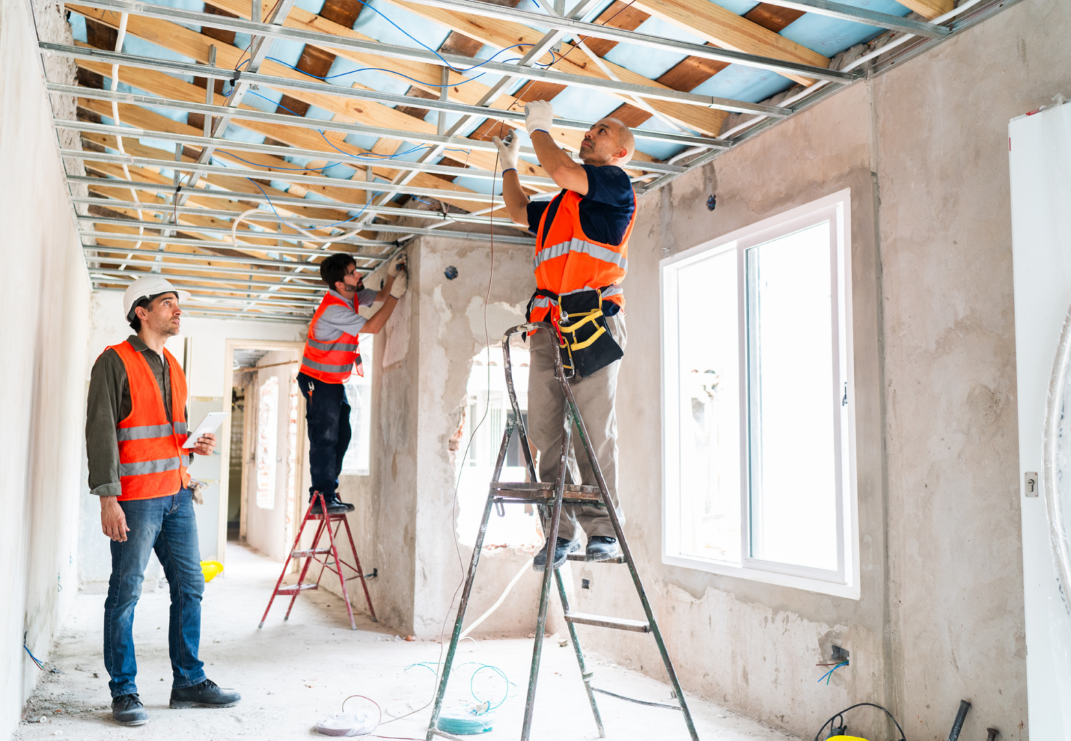 Construction workers installing ceiling framework indoors.