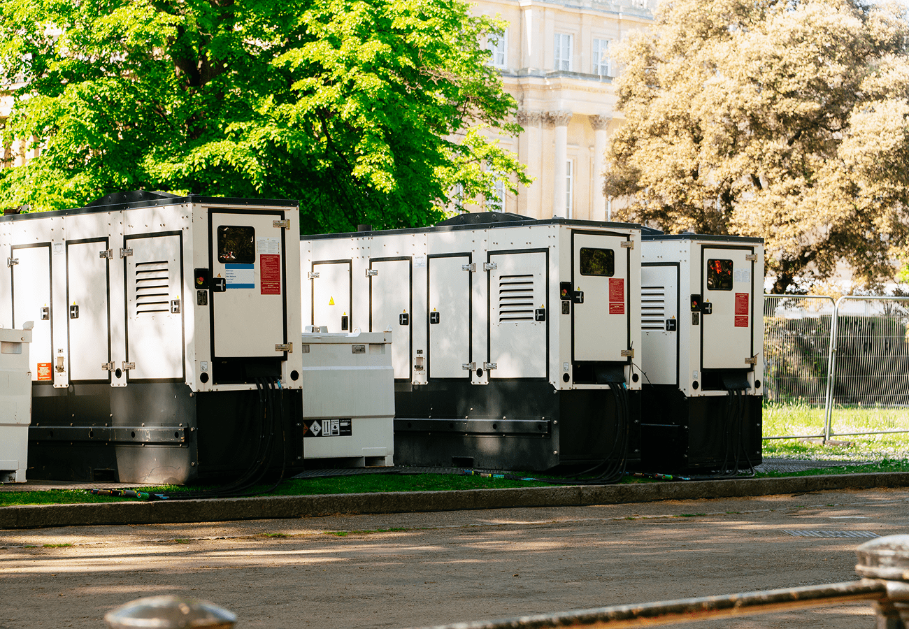 Generators lined up outdoors near trees.