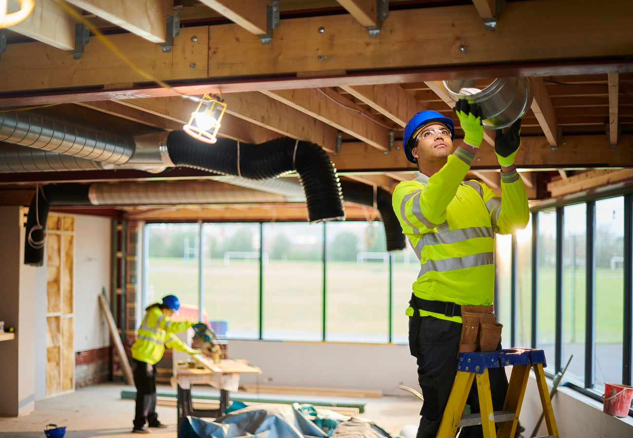Construction workers installing ventilation in building.