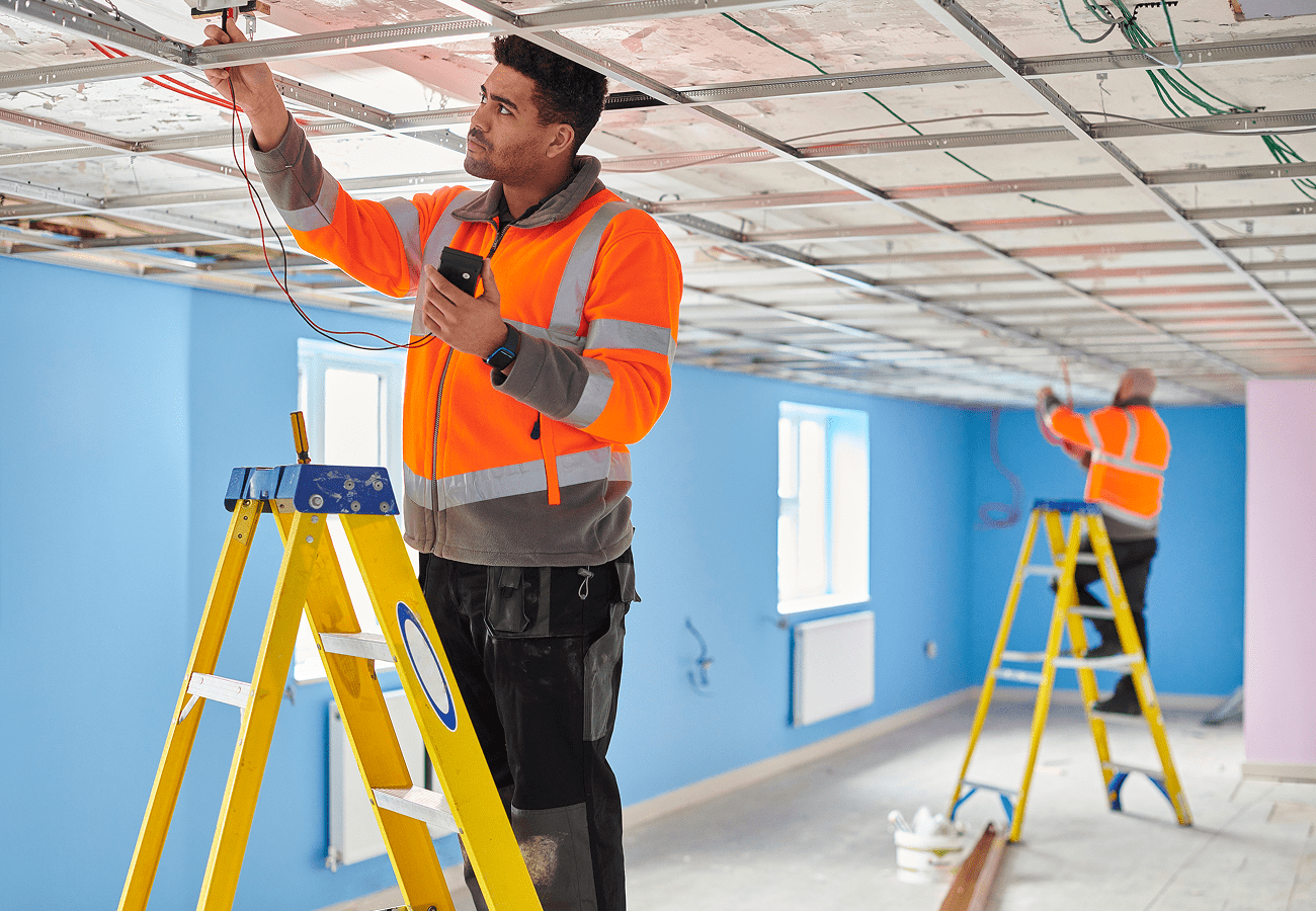 Workers installing ceiling wiring on ladders.