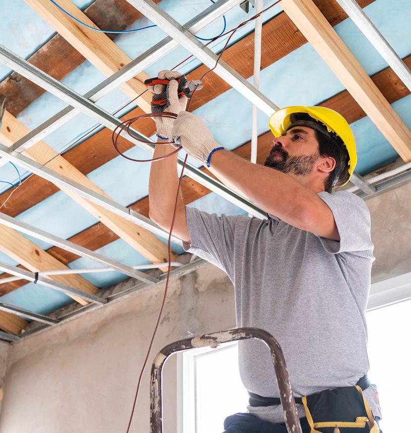 Electrician fixing wires on ceiling framework.