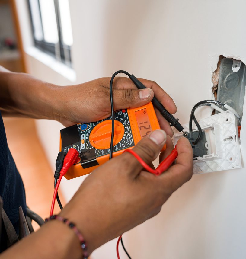 Person using multimeter to check wall socket.