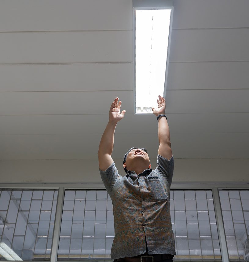 Man reaching towards bright ceiling light.