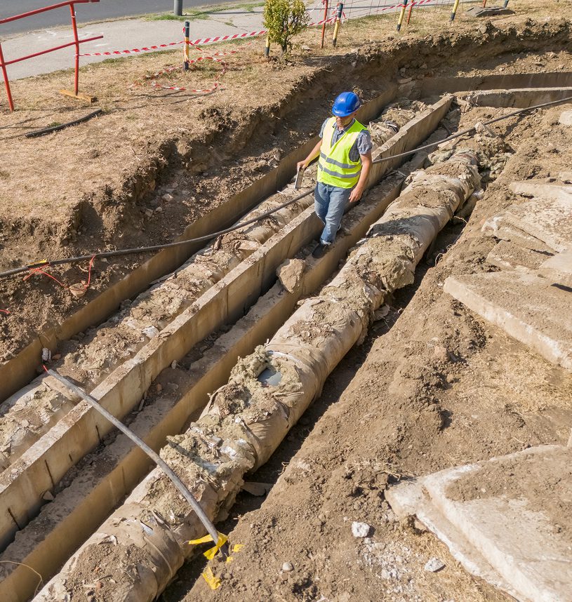 Worker inspecting underground pipes at construction site.